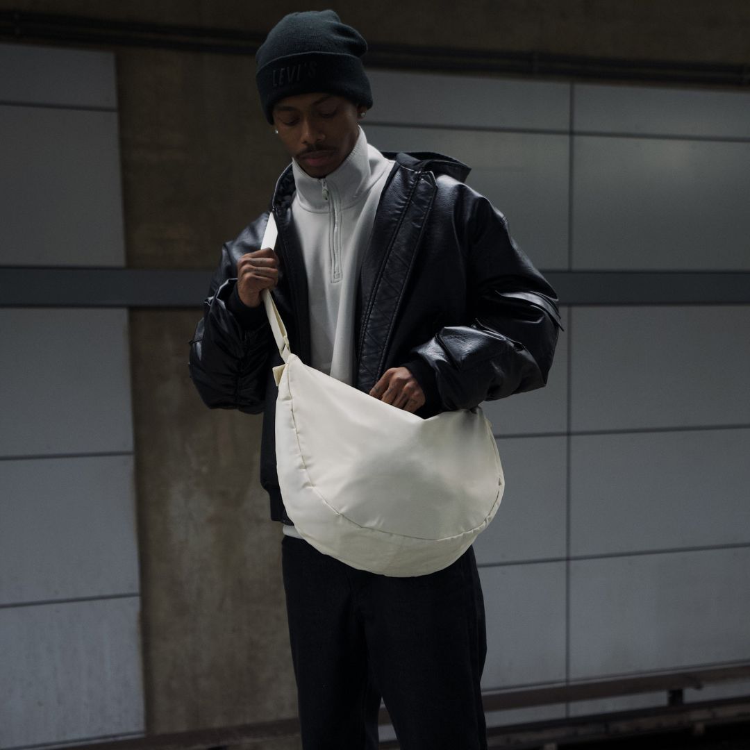 Moon Bag XL beige moodbild outdoor mann steht am bahnhof traegt weißen pulli und schwarze jacke