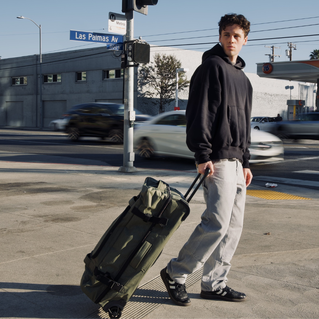 Moodbild Reisetasche mit Rollen Olive gruen KANE Mann zieht draußen den Rollkoffer hintersich