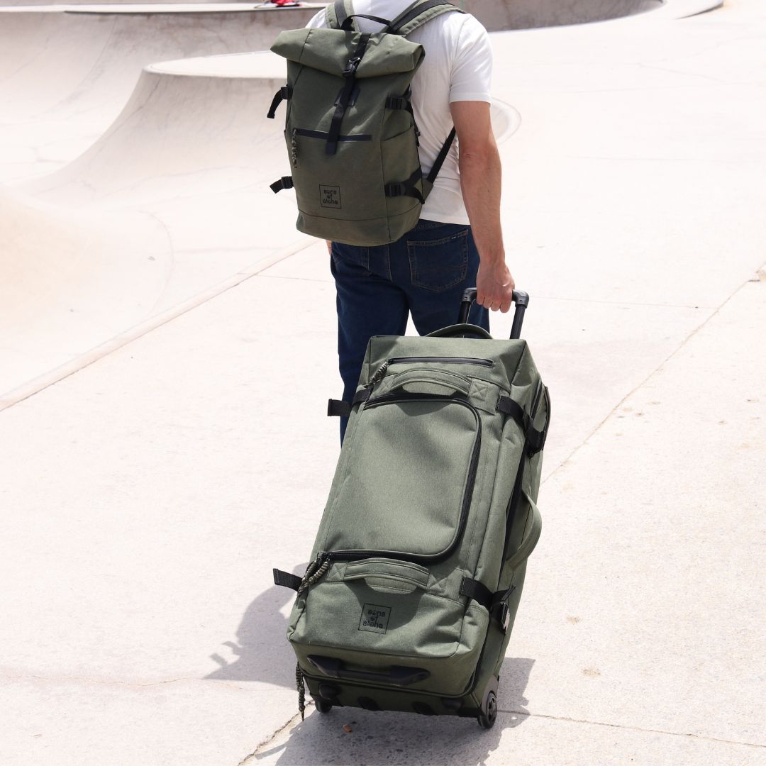 Outdoor Mann geht über einen Skaterplatz und zieht hinter sich den Rollkoffer mit Rollen in grün