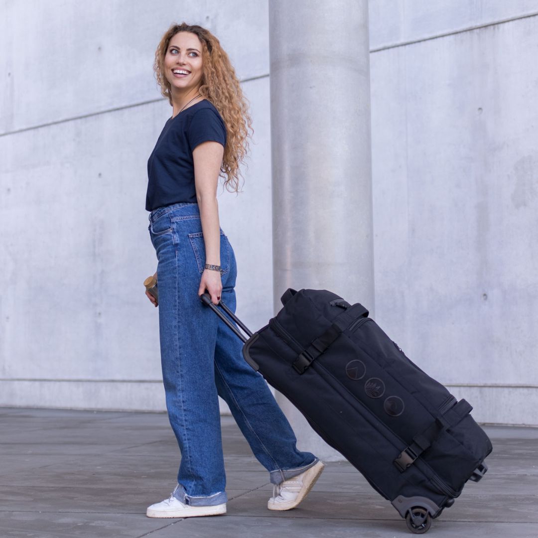 Outdoor Frau geht über einen Platz und zieht hinter sich die Reisetasche mit Rollen in schwarz