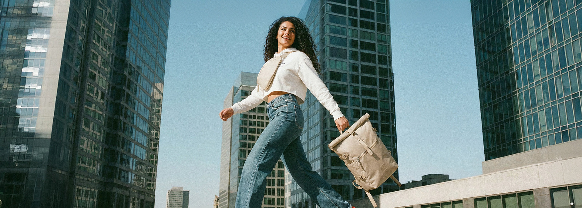 Eine junge Frau im Wald mit Rolltop Rucksack KANE und Reisetasche mit Rollen KANE