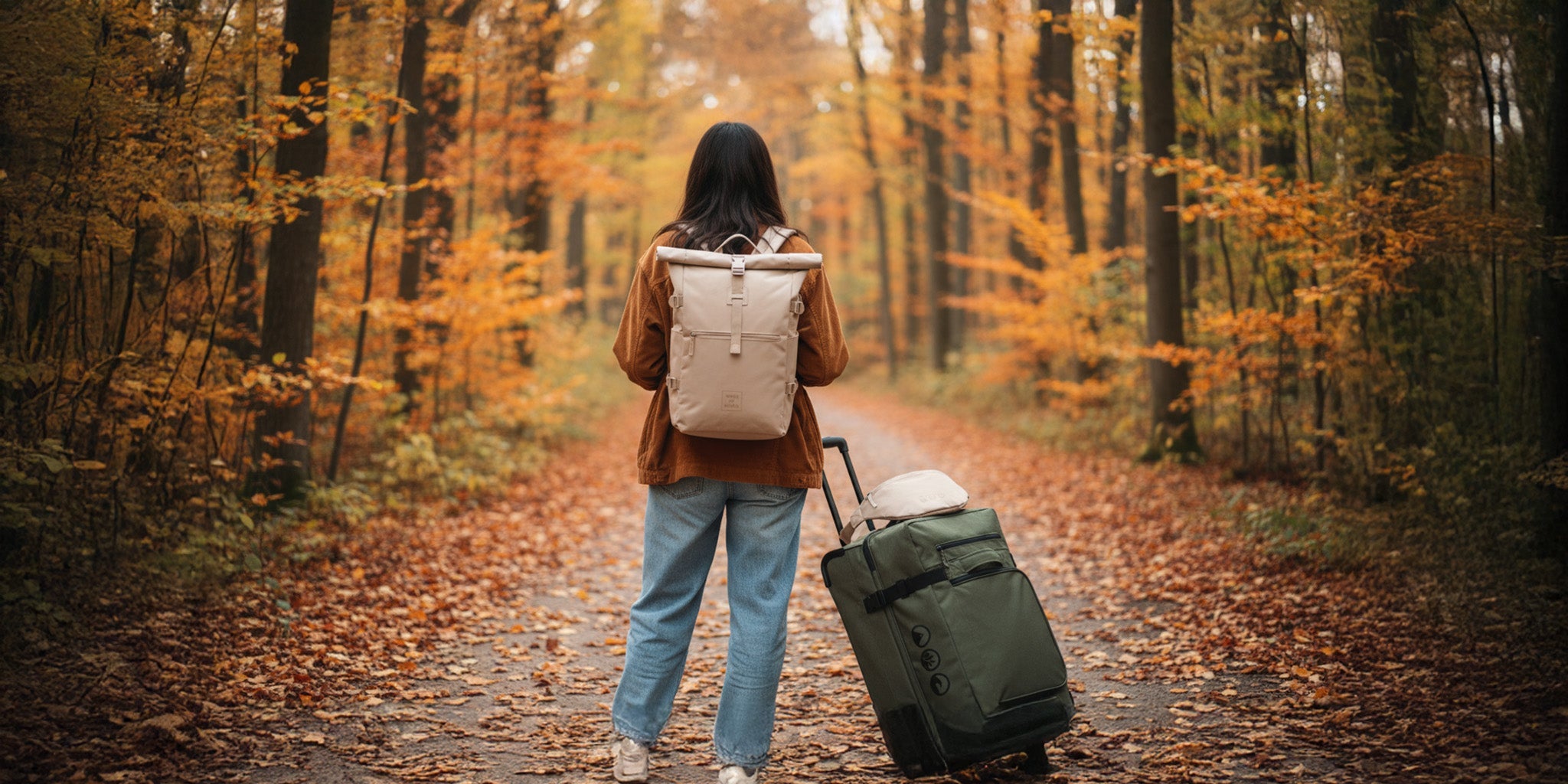 Eine junge Frau im Wald mit Rolltop Rucksack KANE und Reisetasche mit Rollen KANE
